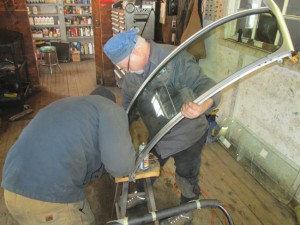 Patrick & Butch wrestle new glass into an MGB windshield frame